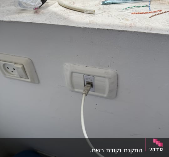 כבל רשת מחובר לשקע בקיר עם חוטים נוספים